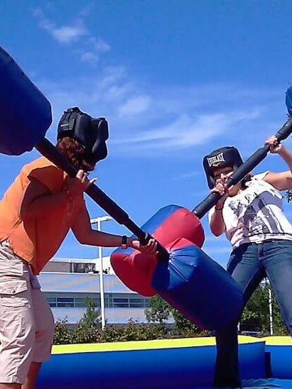 2 people on blue inflatable fighting with huge inflatable bars in gladiator joust team building event