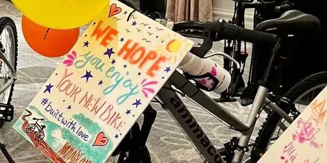 Black push bike decorated with balloons and a hand written sign