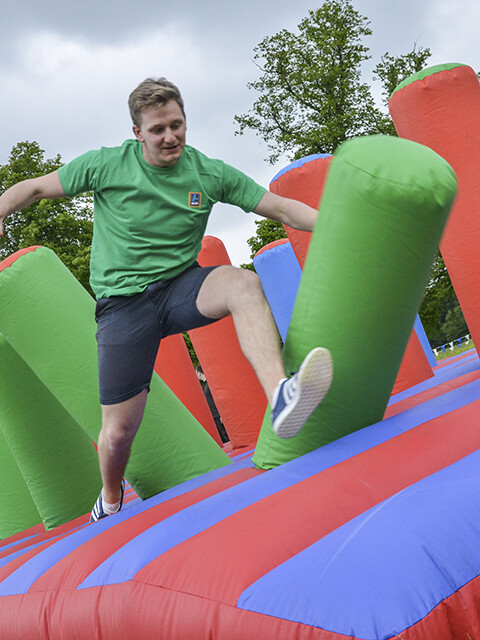 Man jumping on colourful inflatable assault course in outdoor summer team building event