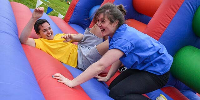 Two colleagues laughing on a giantn inflatable assault course