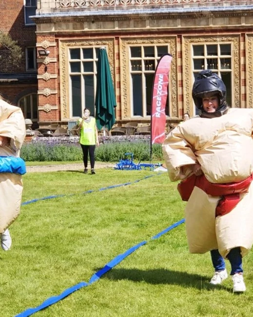 Women in inflatable sumo costumes racing along green pitch in outdoor team building event