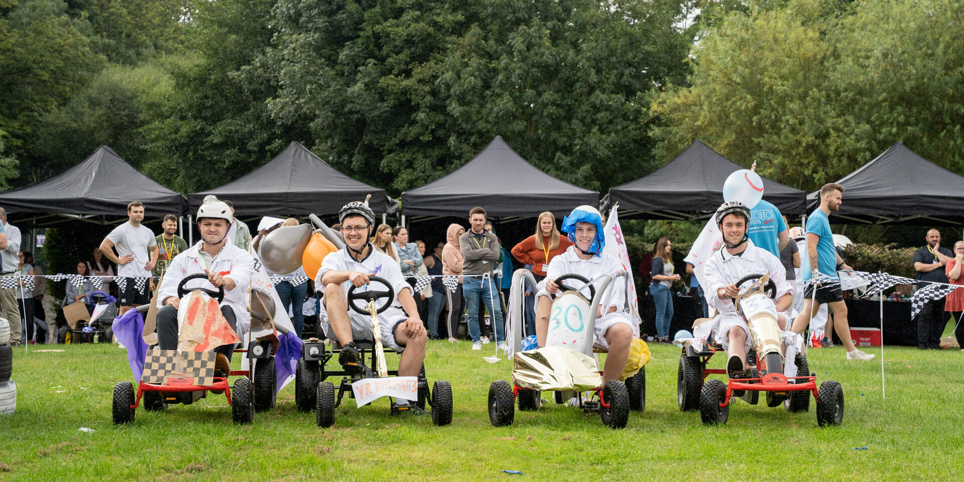 people with funny hats driving soapbox cars in outdoor team building activity