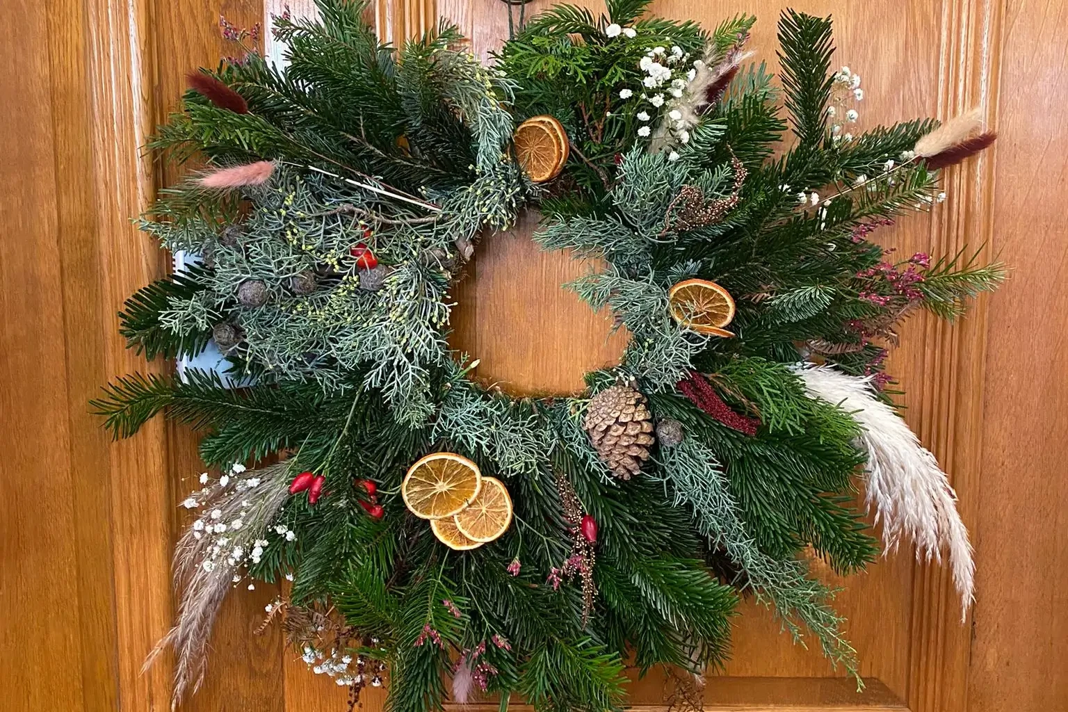 Christmas Wreath with pine cones and dried oranges hanging on a wooden door