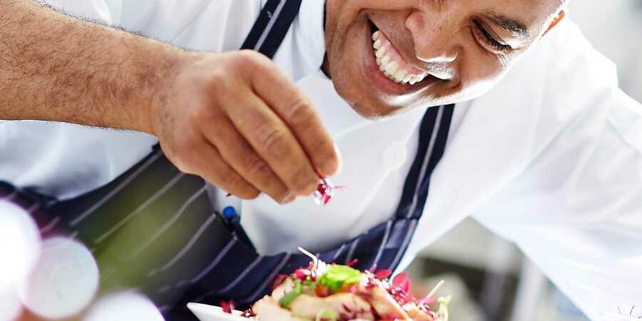 Chef sprinking the finishing garnish onto a plate of food