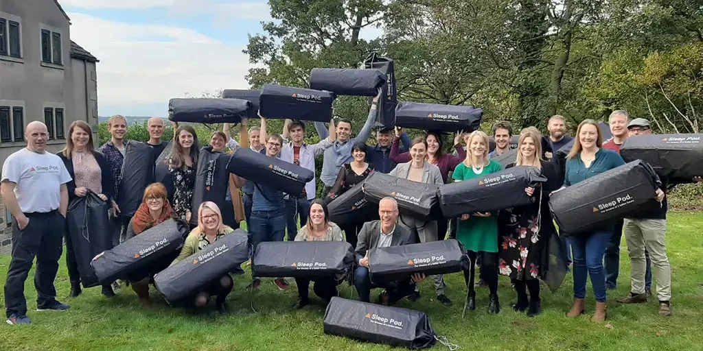 sleep pods charity team building participants holding sleep pod bags outdoors