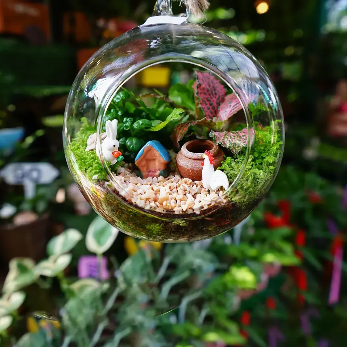 glass terrarium hanging with cute miniature figurines on dark greenery background