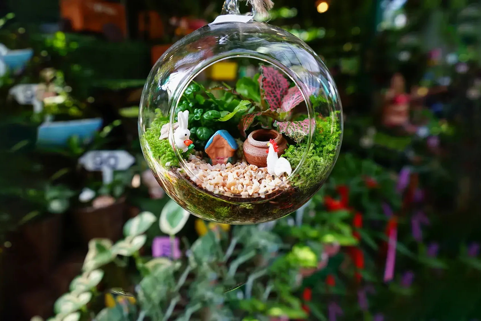 glass terrarium hanging with cute miniature figurines on dark greenery background