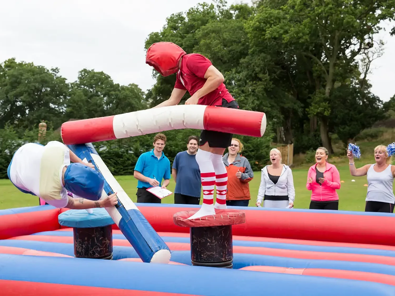 gladiators on inflatable arena fighting with corlourful pugil sticks in team building event