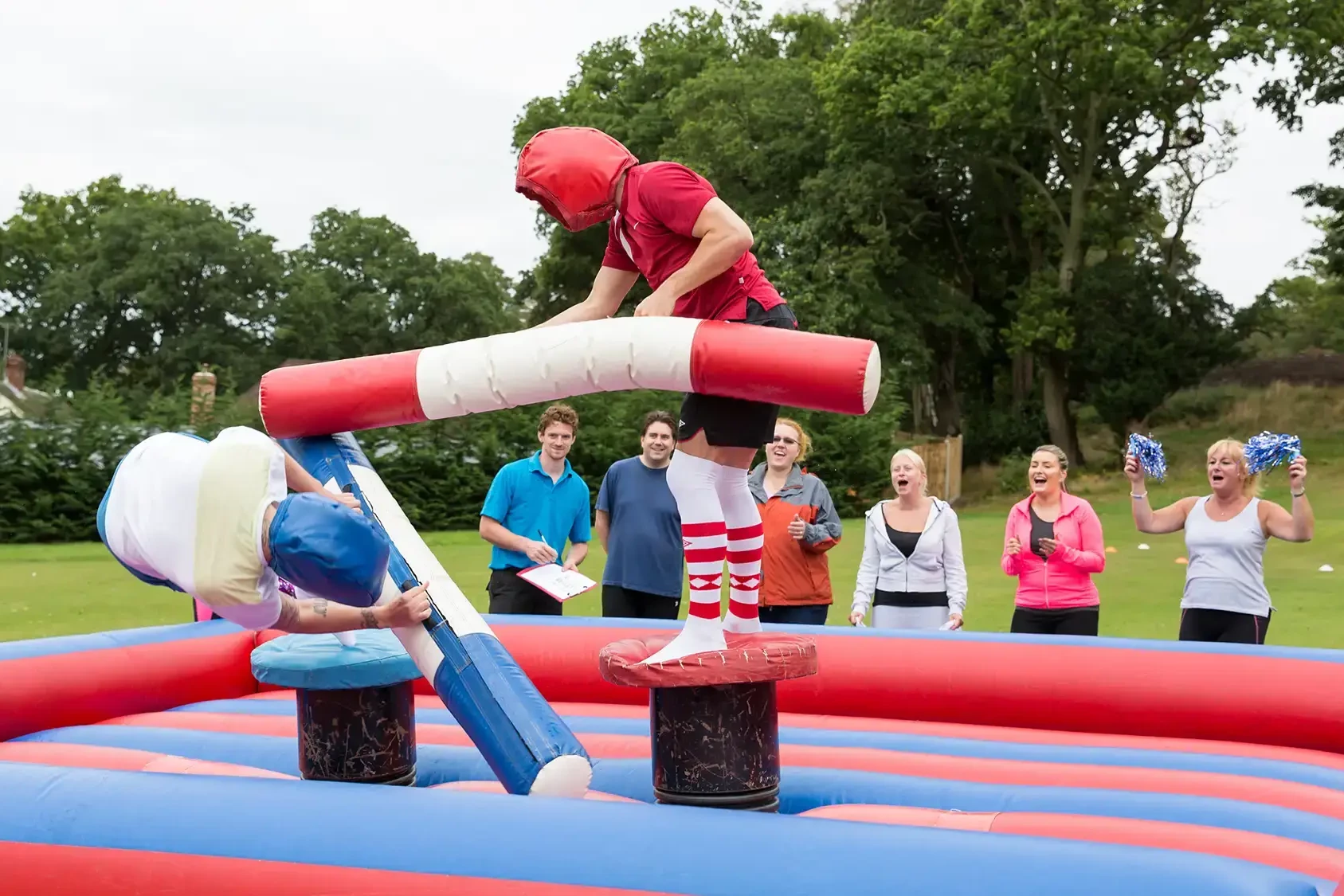 gladiators on inflatable arena fighting with corlourful pugil sticks in team building event