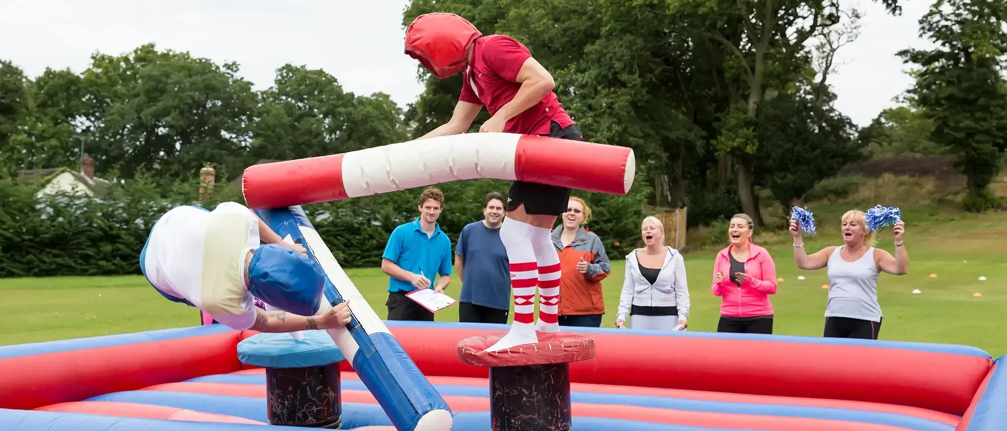 gladiators on inflatable arena fighting with corlourful pugil sticks in team building event