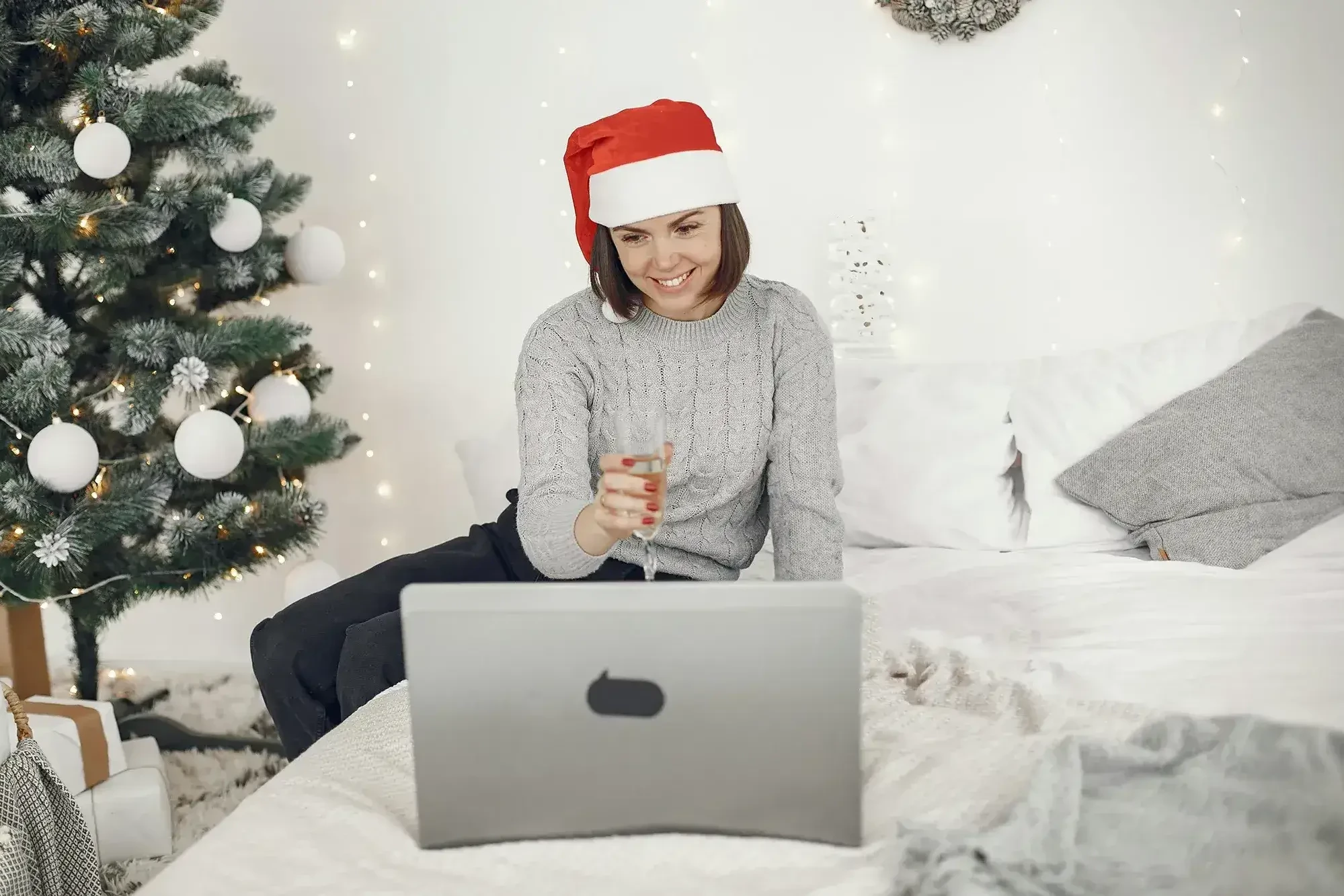 women holding a glass of champagne and wearing a Christmas hat in front of laptop while participating in virtual Christmas party