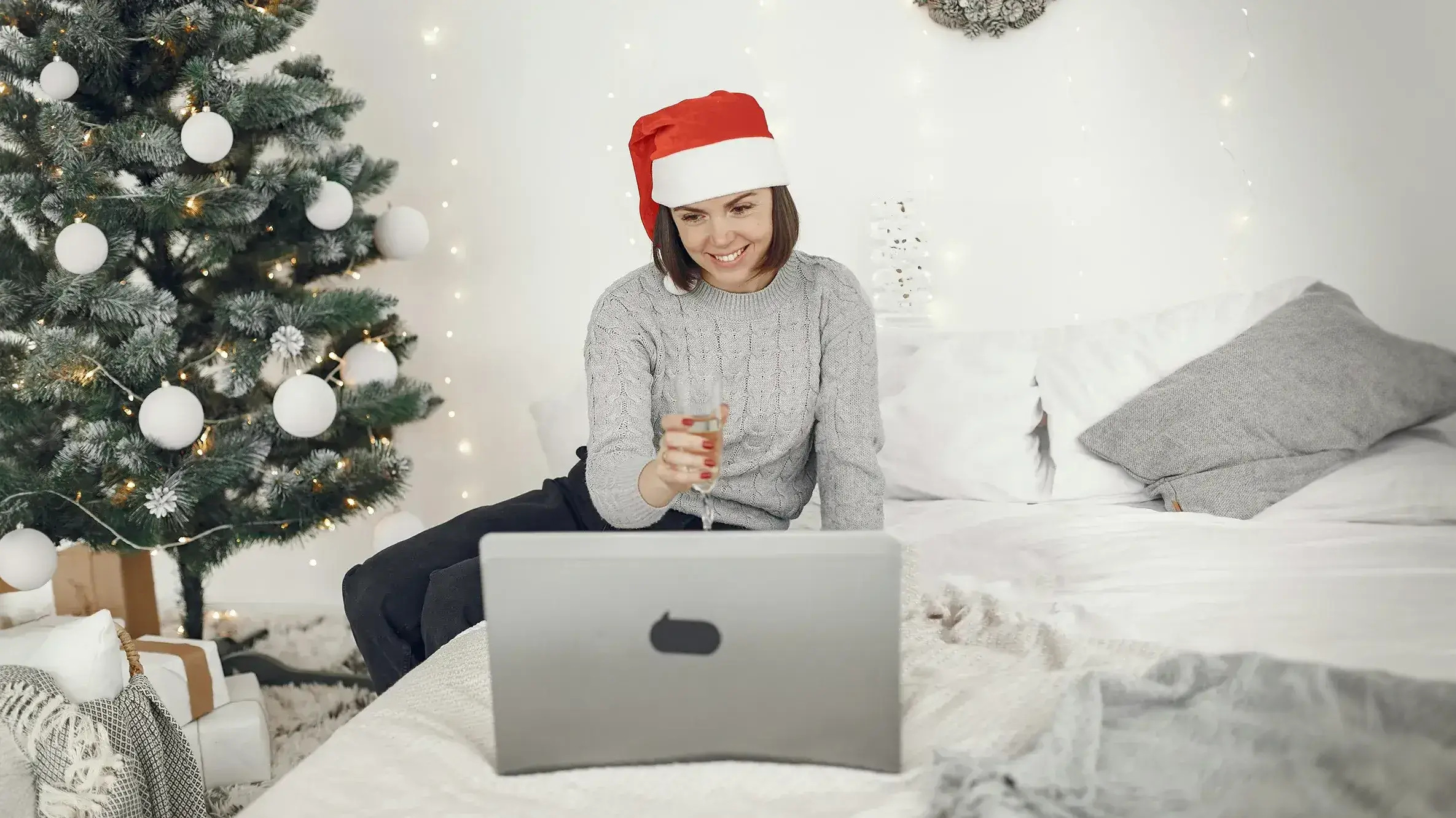 women holding a glass of champagne and wearing a Christmas hat in front of laptop while participating in virtual Christmas party